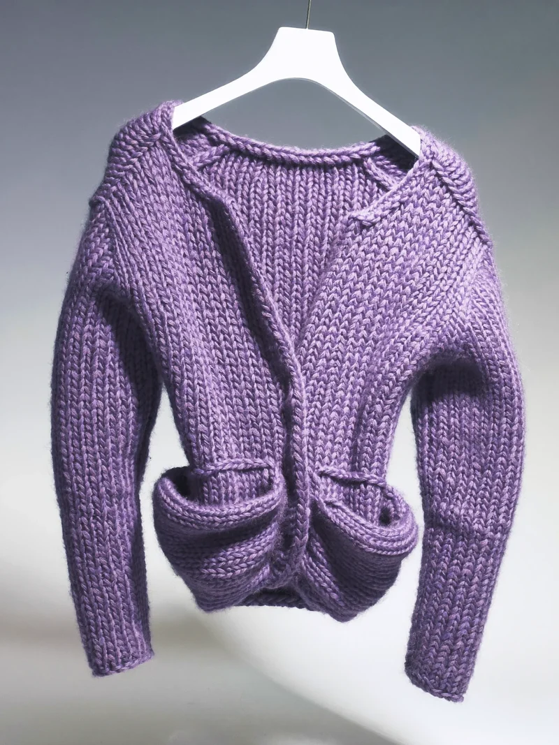 Studio illustrato di cardigan in maglia scultorea appeso a una gruccia neutra